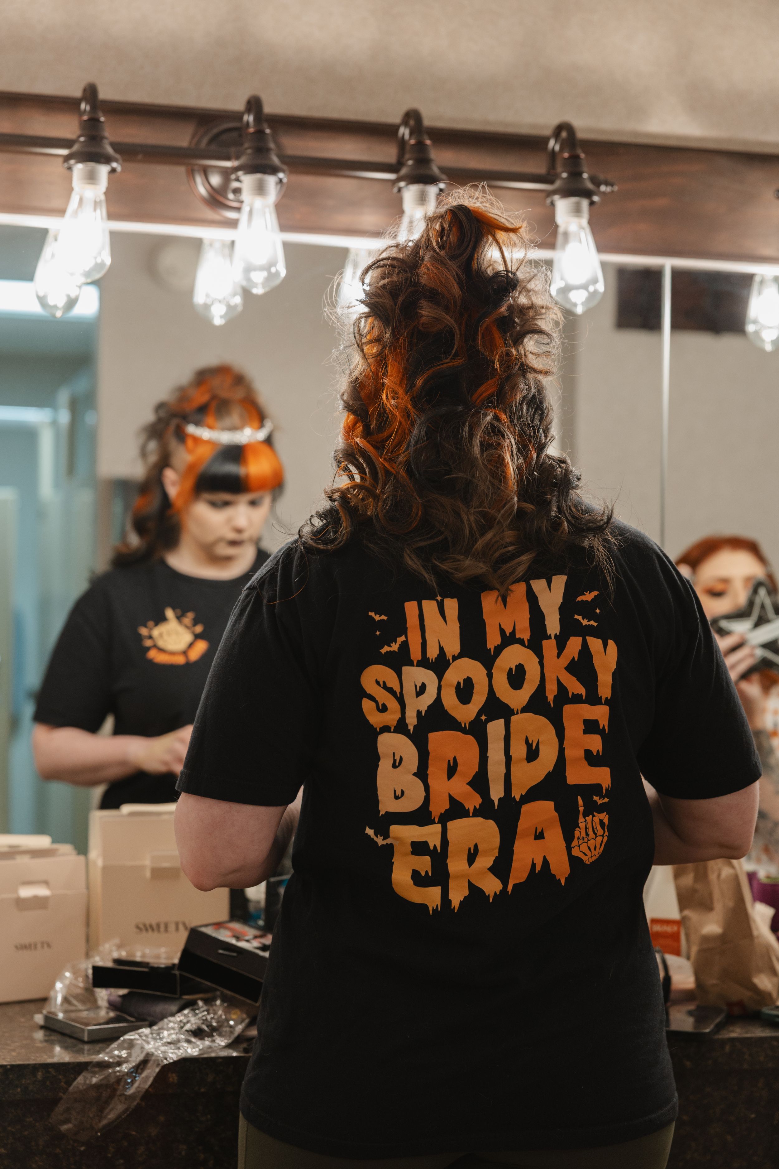 Black t-shirts with Halloween themed text in orange lettering displayed in a dressing room mirror.