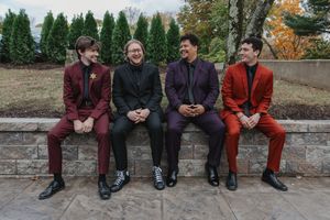 Four people sit on a stone wall wearing coordinated burgundy and black outfits in an outdoor setting.