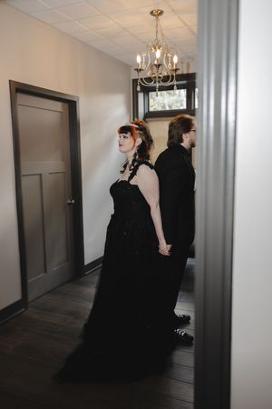 Elegant black gowns sweep through a hallway with chandelier lighting and modern decor.