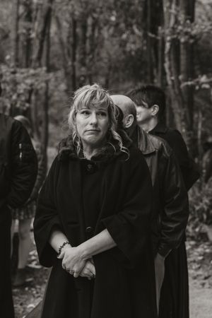 A couple dressed in black poses together in a wooded outdoor setting for moody portrait photos.