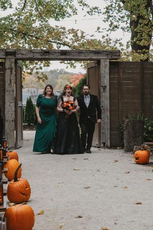 Wedding party stands by wooden fence with carved pumpkins creating festive Halloween atmosphere.