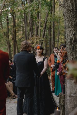 Outdoor forest wedding ceremony with autumn decor and orange fabric accents.