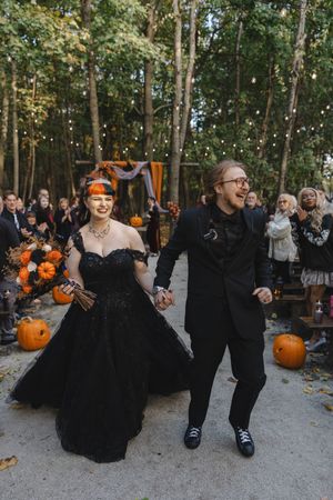 A Halloween-themed wedding celebration with black attire and orange pumpkin decorations in a forest setting.
