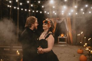 String lights illuminate a romantic outdoor autumn wedding reception with glowing lanterns and pumpkin decor at dusk.