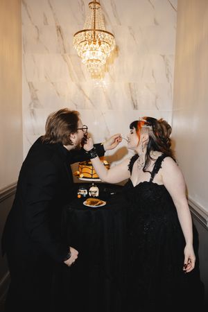 A group in black formal attire gathered around a table with elegant crystal chandeliers overhead.