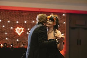 A couple shares a romantic dance moment under red lighting with a heart-shaped light display in the background.