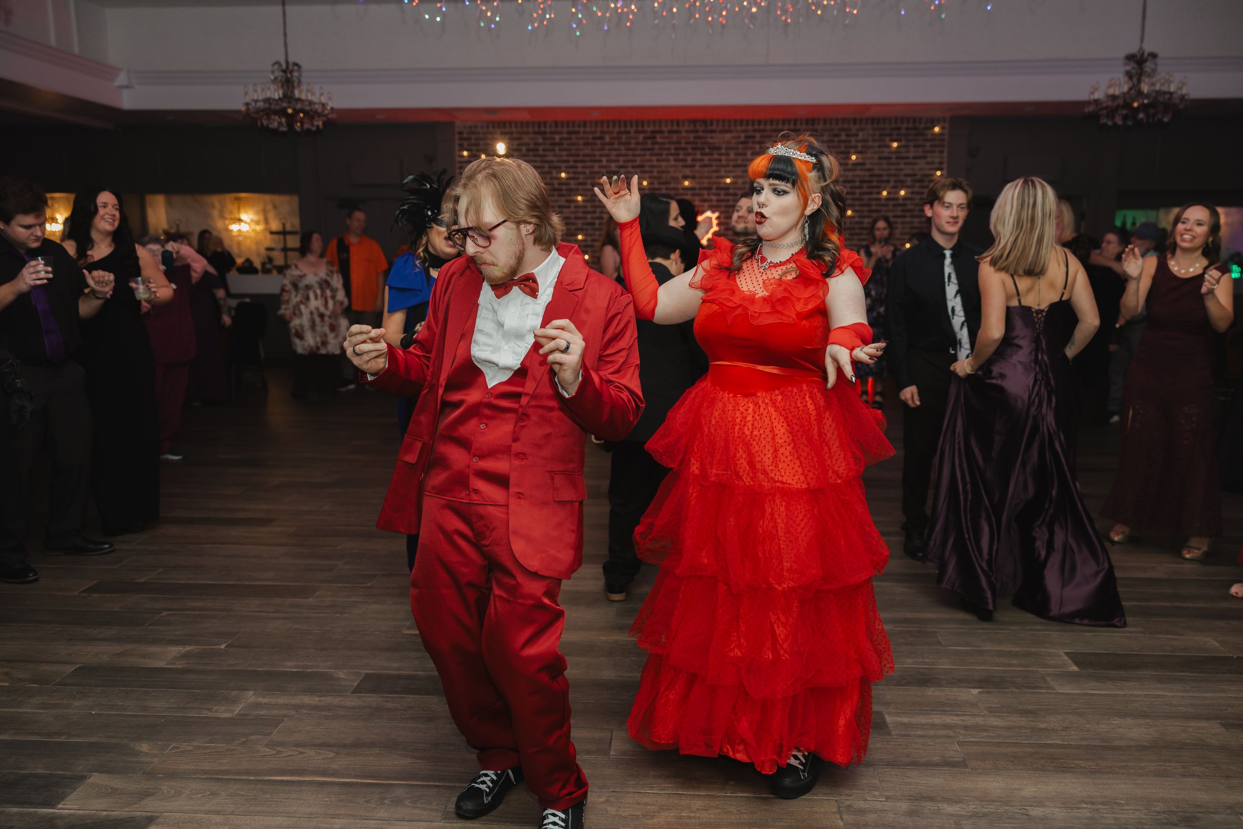 Wedding reception dance floor with couples in formal attire under dim lighting.
