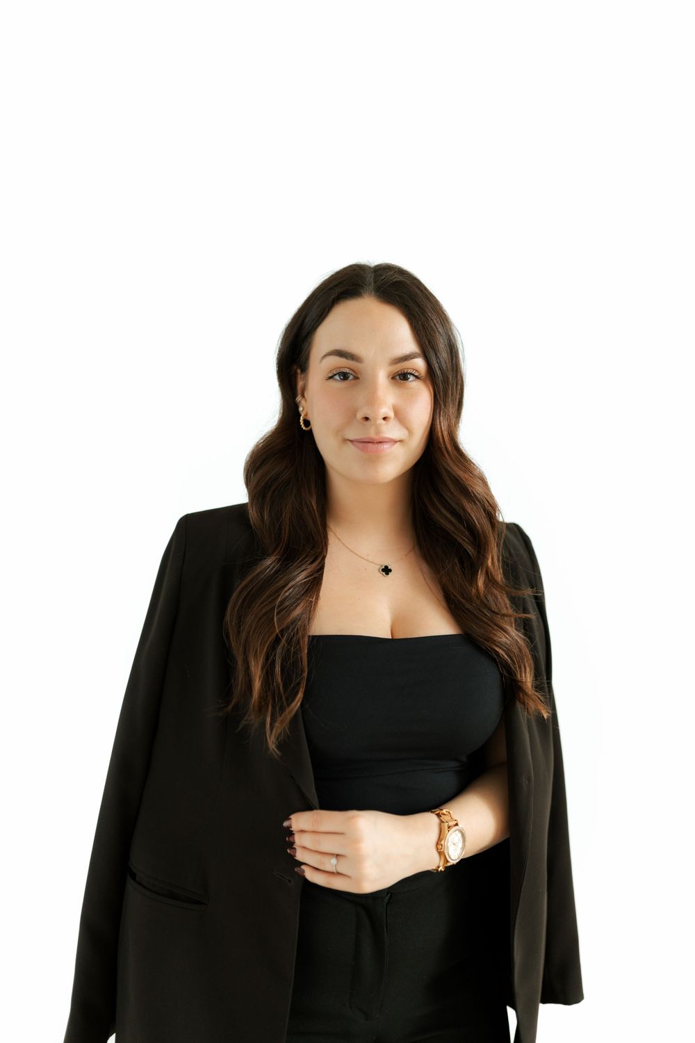 Confident brunette woman in black blazer and strapless top posing on white background.