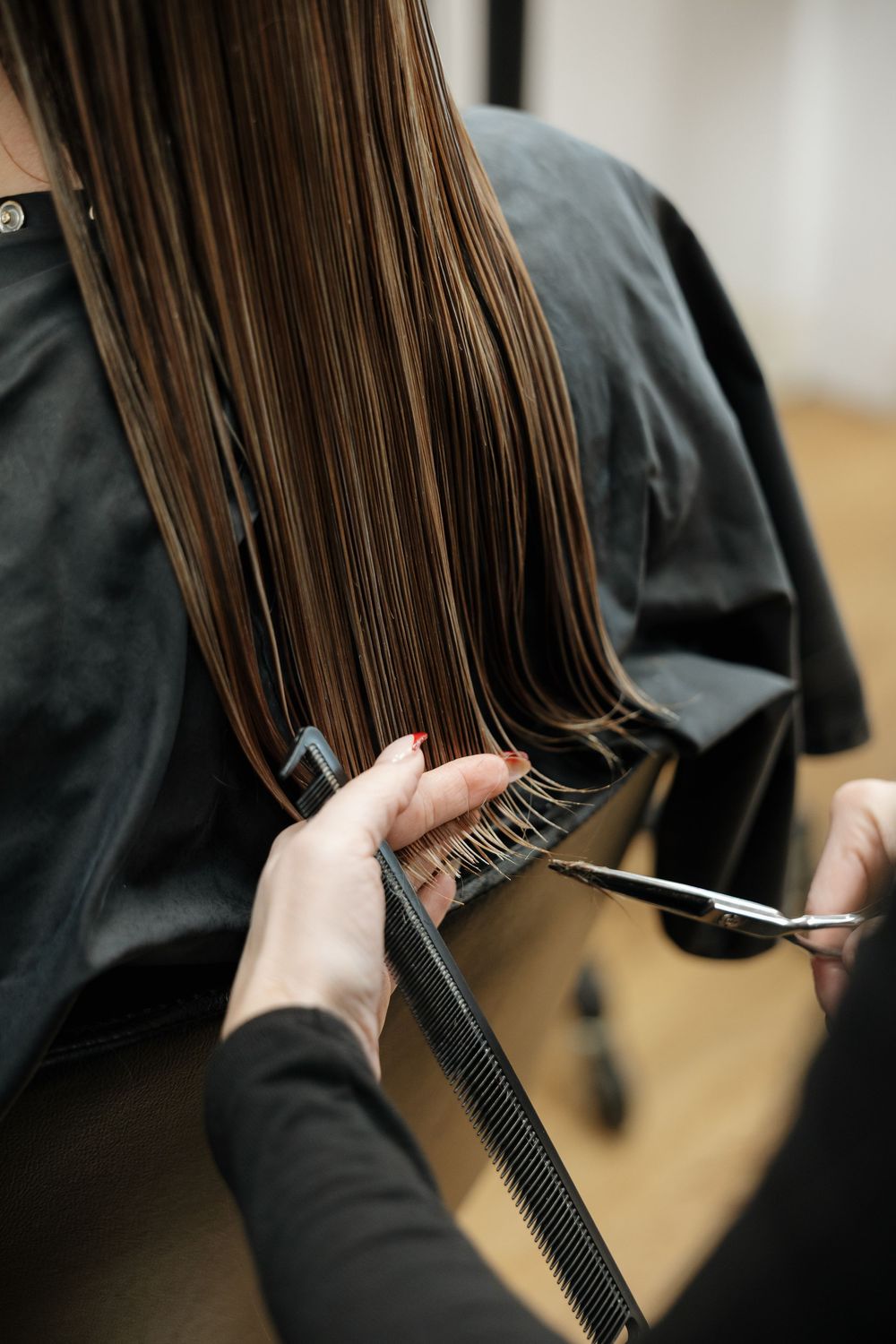 Hairstylist trimming long straight brown hair with scissors and comb in salon.