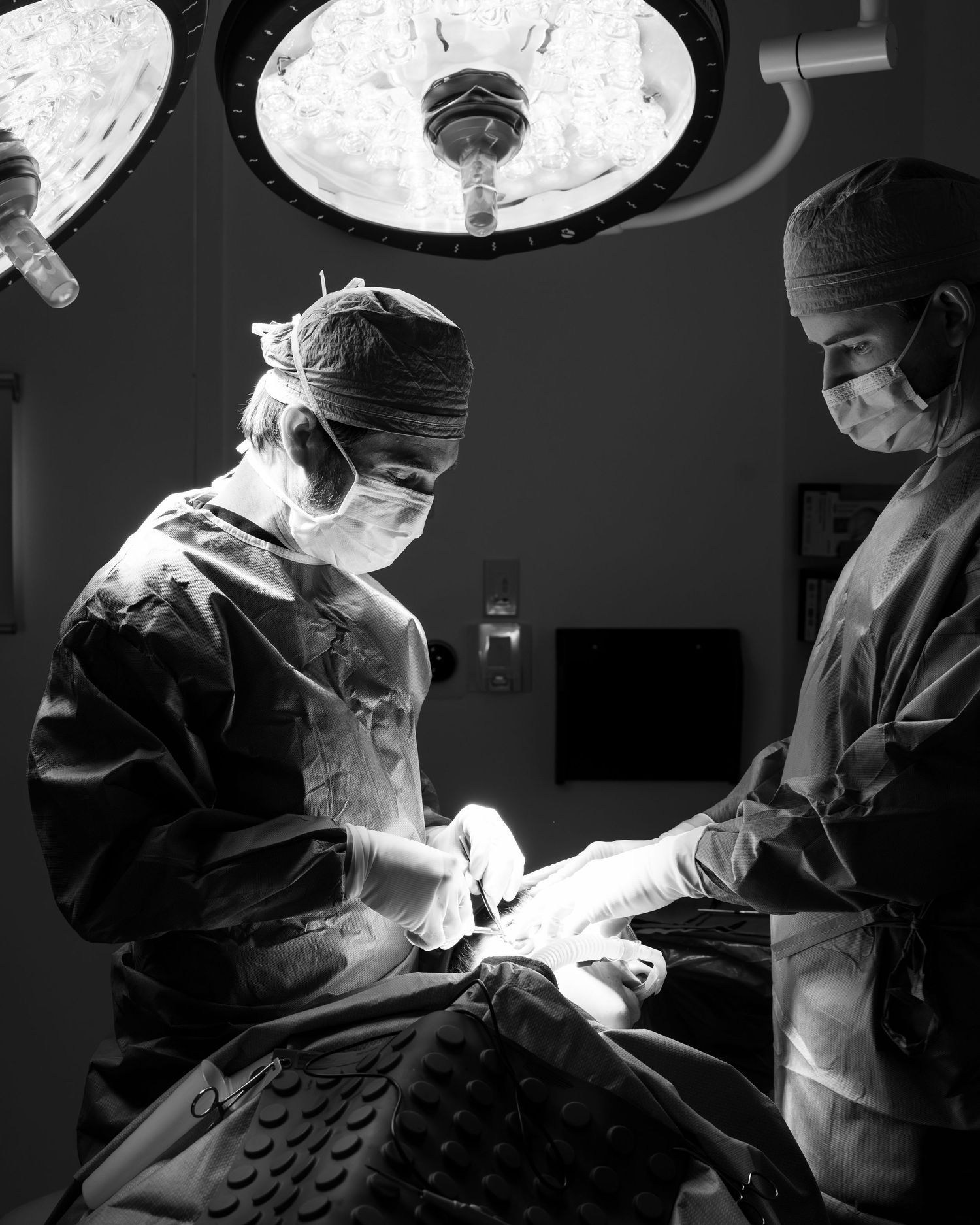 Medical professionals perform surgery in an operating room under bright surgical lights in black and white.