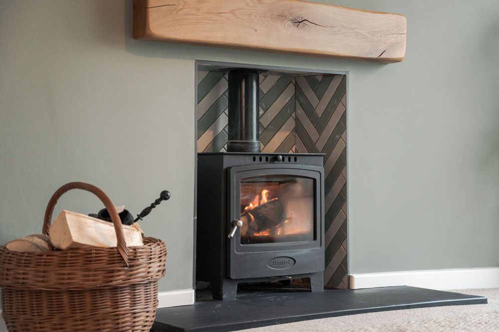 Rustic fireplace setup with woven basket and wooden mantel against herringbone pattern tile backdrop.