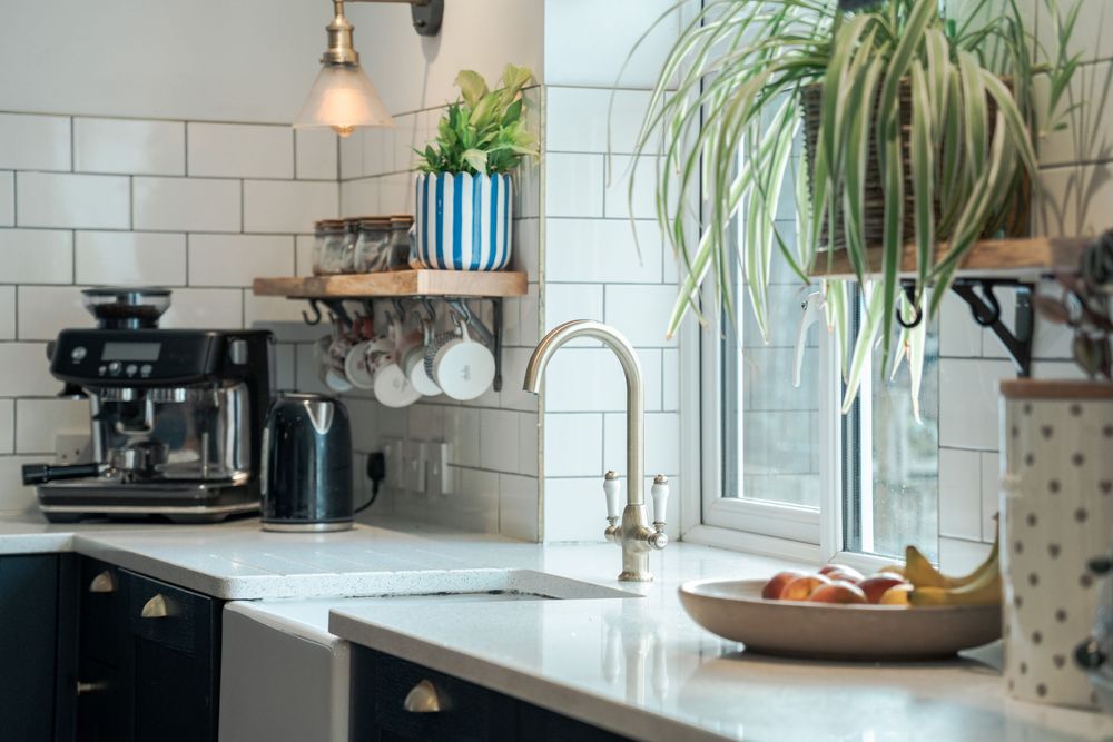Contemporary kitchen featuring white tiles, hanging plants, and natural light from windows.