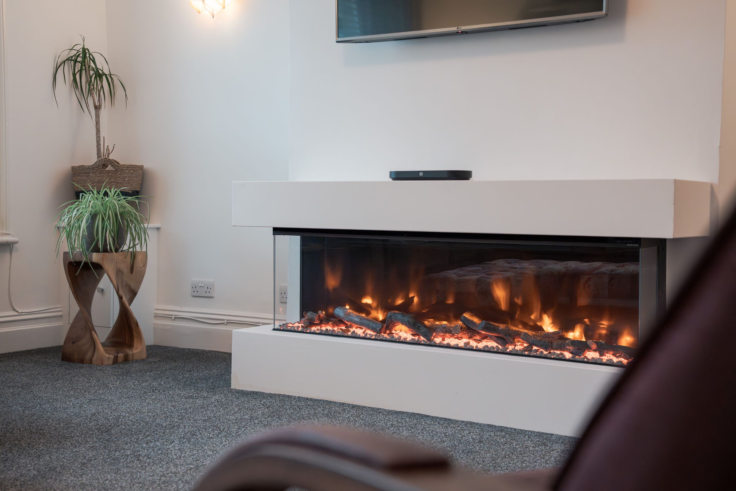 Contemporary living space featuring a wall-mounted TV above a sleek electric fireplace with orange flames.