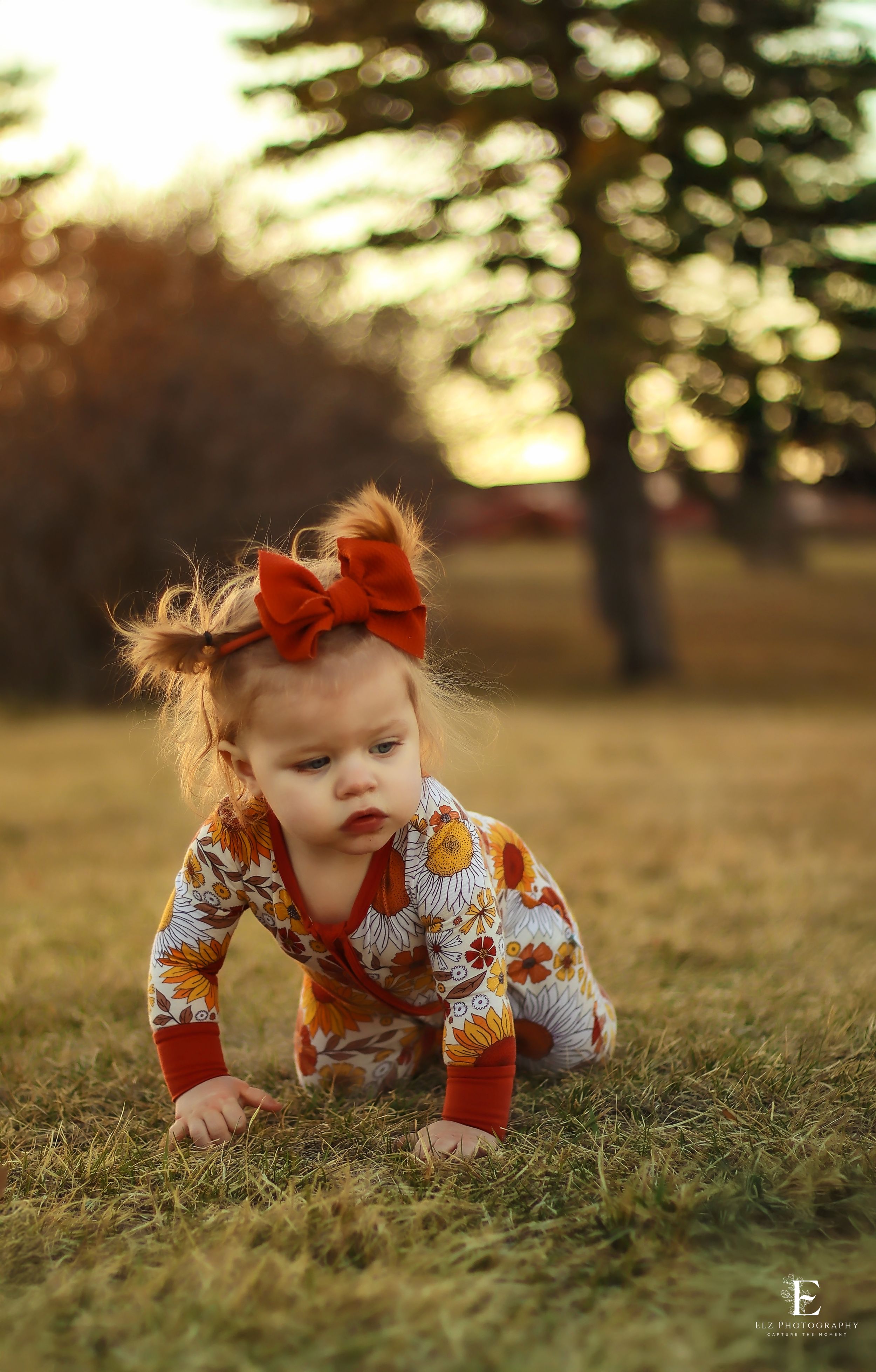 Small child in floral outfit crawling on autumn grass during sunset in Williston, North Dakota.