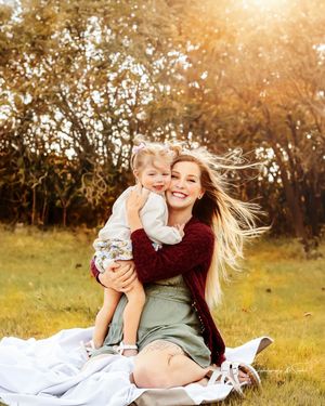 Mom and daughter sitting on a blanket backlit by sun and all the greenery around them in Williston, North Dakota.