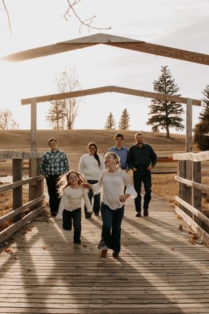 People walking across a wooden bridge with evergreen trees in the background during golden hour in Williston, North Dakota.