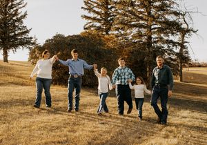 A group walking together through a grassy field with pine trees in the background at sunset in Williston, North Dakota.