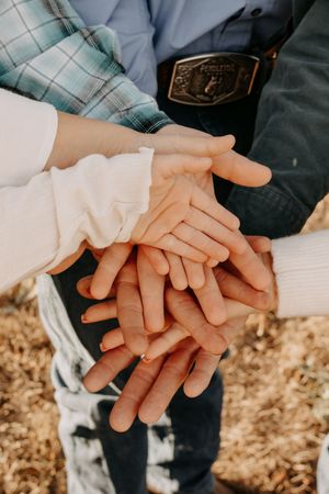Multiple hands stacked on top of each other in a unity gesture against a natural background in Williston, North Dakota.