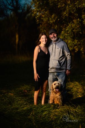 Couple poses with their small dog in tall grass during evening photoshoot in Pierre, South Dakota.