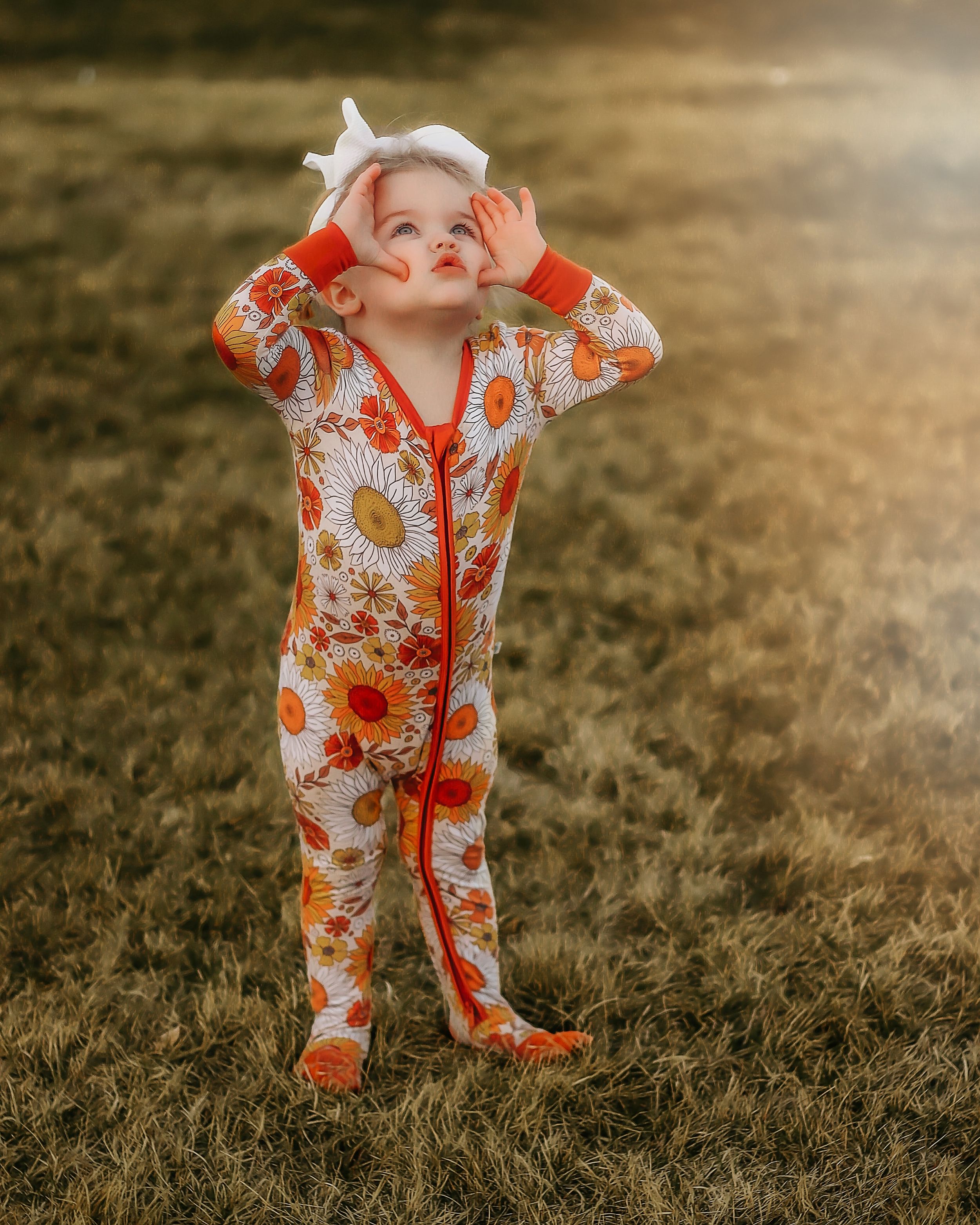 Baby wearing floral print onesie walking on grass during golden hour sunset in Williston, North Dakota.