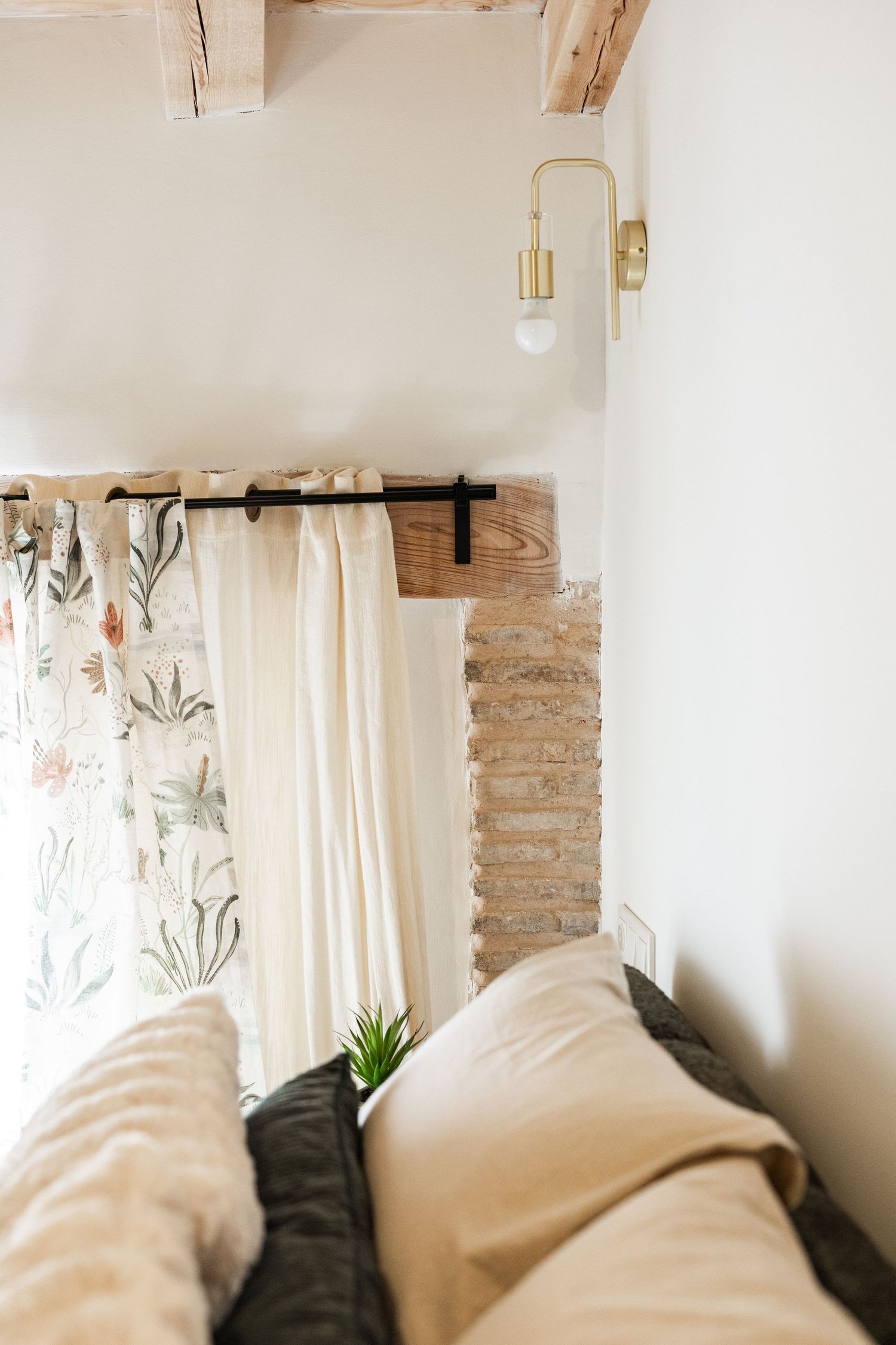 Modern bedroom interior with white walls, floral curtains, brass wall sconce, and cozy neutral bedding.