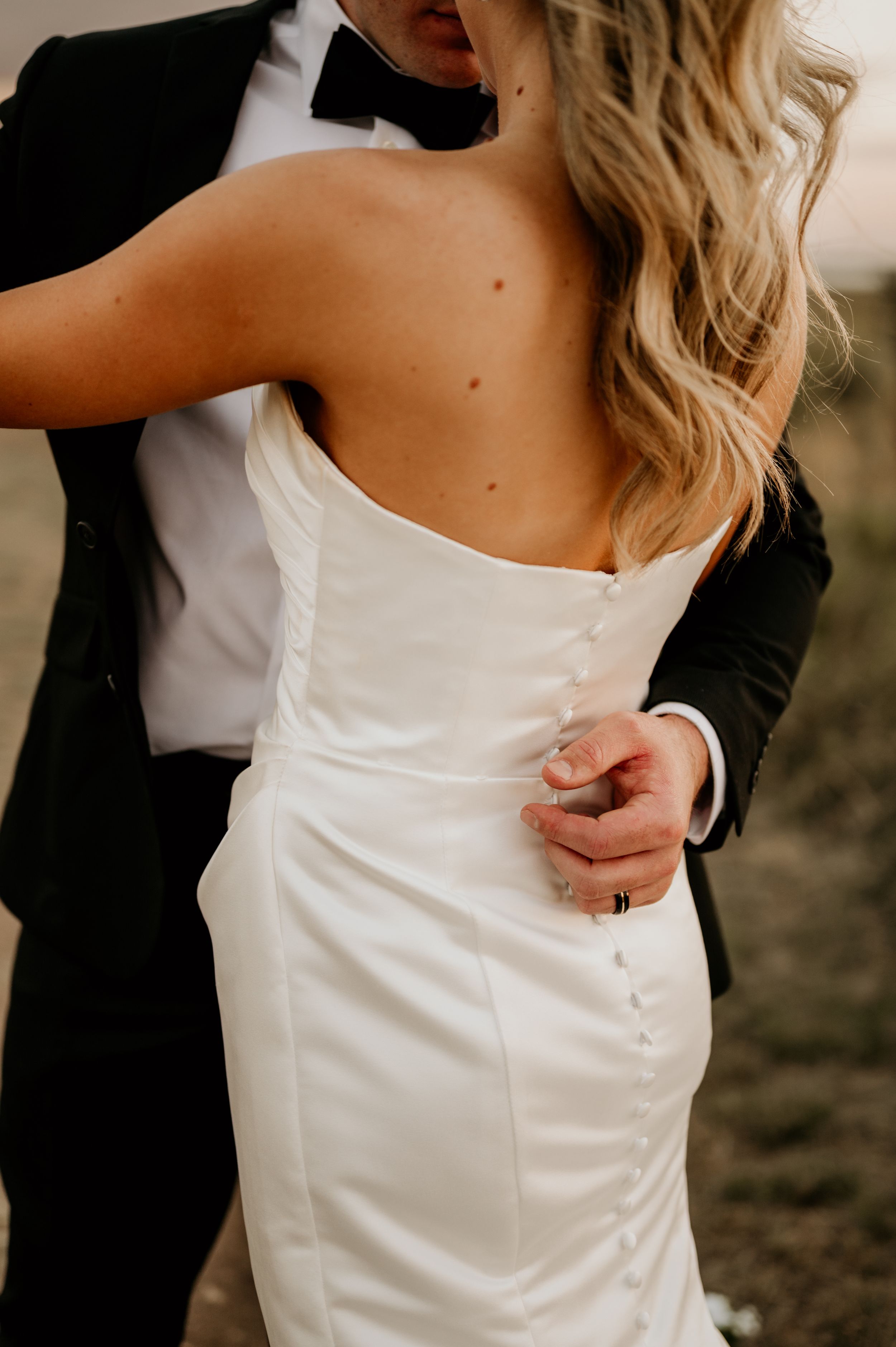 Close-up details of a white wedding dress being buttoned up.