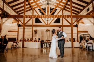 Wedding reception in a rustic wooden barn venue with exposed beams and chandeliers.