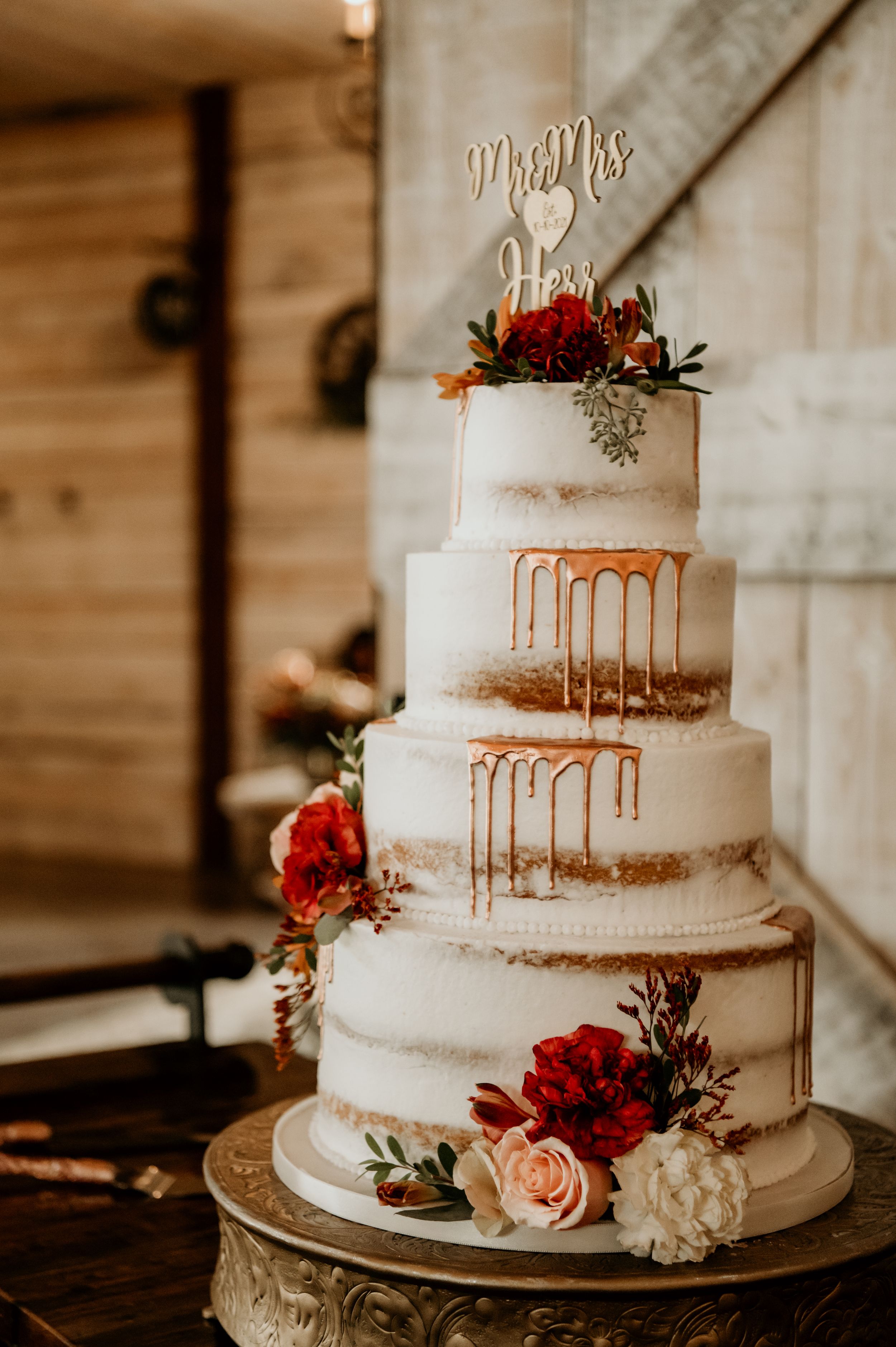 Three-tiered semi-naked wedding cake decorated with roses and gold drip details.