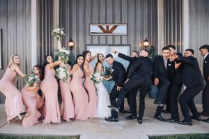 Wedding party in pink dresses and black suits posing playfully on the ground.