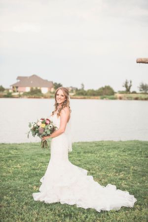 Bride in flowing white dress poses gracefully in a sunlit meadow with her bouquet.