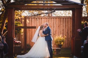 Romantic wedding couple shares intimate moment under rustic wooden pergola during sunset.