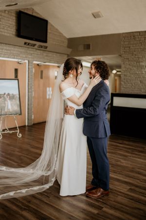 First look moment between couple in an indoor venue with wooden floors and white brick walls.
