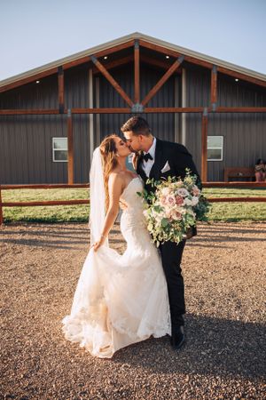 Bride in flowing white gown walks with groom outside rustic barn venue.