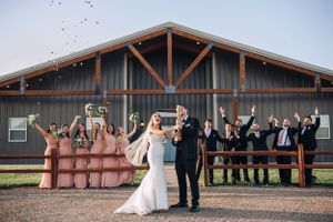 Wedding party poses together in front of rustic barn venue at sunset.