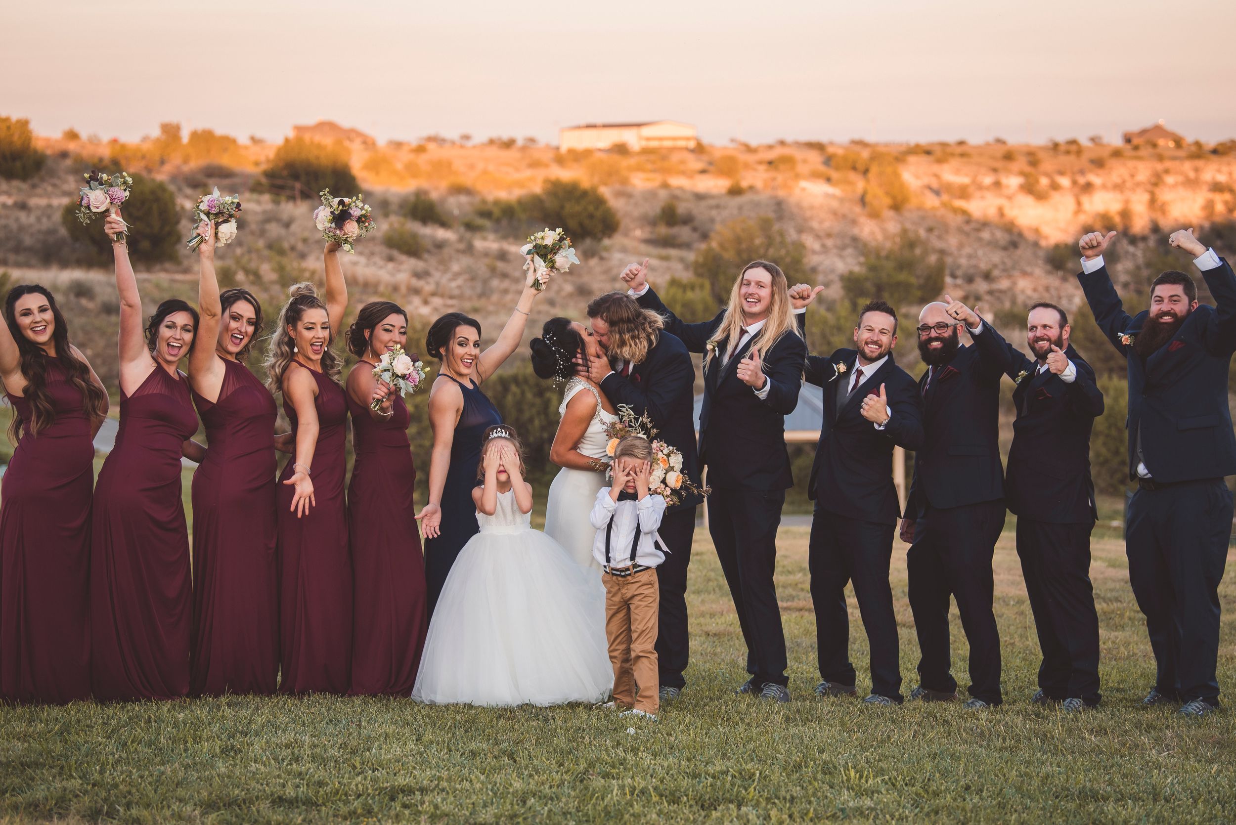 Wedding party lined up at sunset in burgundy and black attire.
