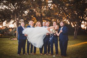 Wedding party poses at sunset with trees silhouetted against golden sky.