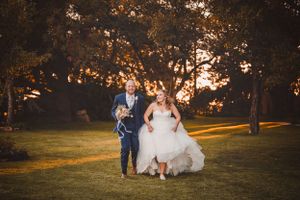 Wedding party runs playfully through a sunlit park at golden hour.