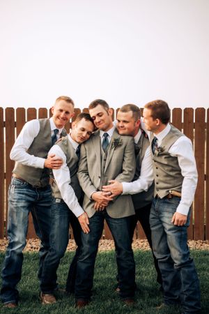 Groomsmen in grey vests and jeans pose playfully in casual group photo.