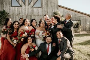Wedding party celebrating and laughing together outside rustic wooden barn.