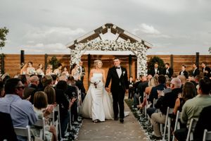 Wedding ceremony in rustic barn venue with wooden walls and floral arch backdrop.