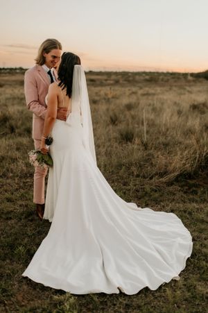 Elegant white wedding dress with flowing train photographed in golden field at sunset.