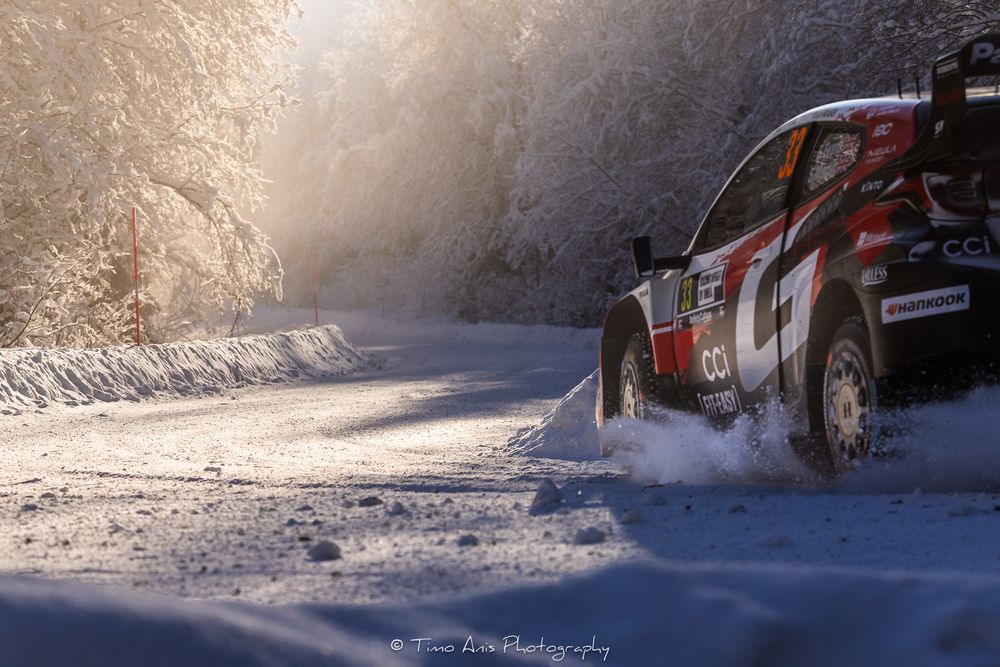 Rally car kicks up snow while racing through a wintry forest course in dramatic action sequence.