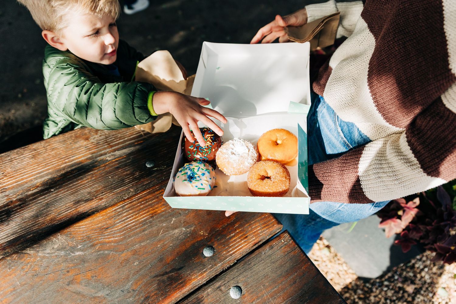 Close-up view of hands holding colorful donuts and coffee cups on a rustic wooden table for Charlotte family photos.
