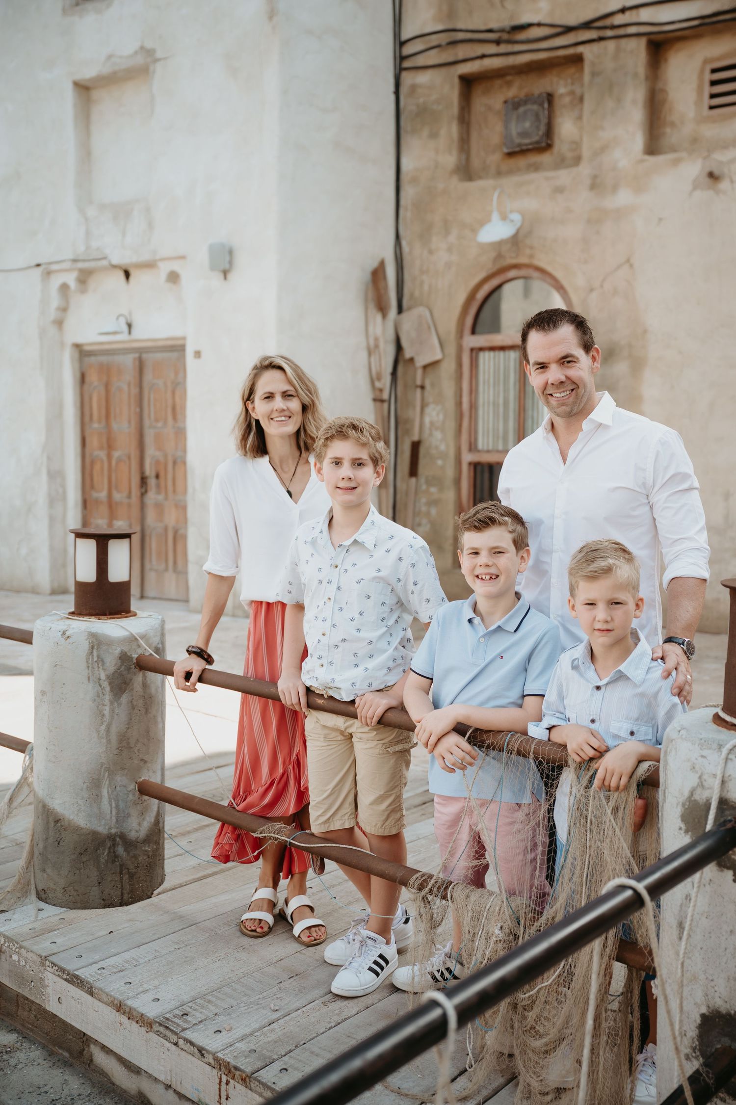 Family group sits together on a rustic concrete wall against a bright turquoise blue door background.