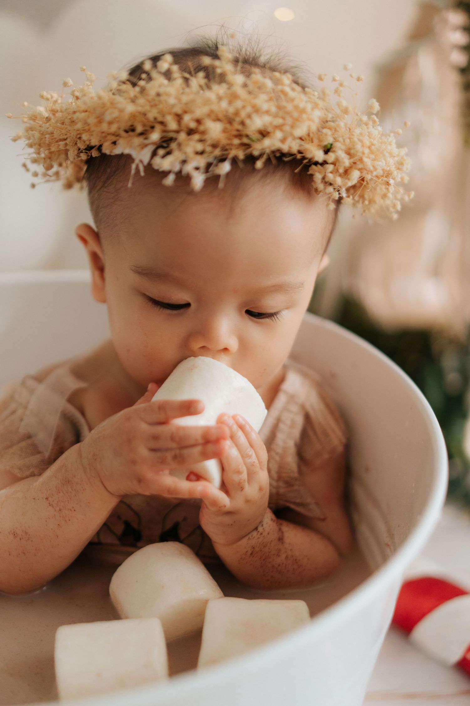 Baby in white outfit plays with colorful pastel balloons and smash cake during first birthday photoshoot.