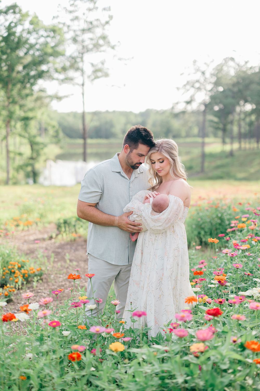 Mom and dad standing in a zinnia field while snuggling and holding their baby closely.
