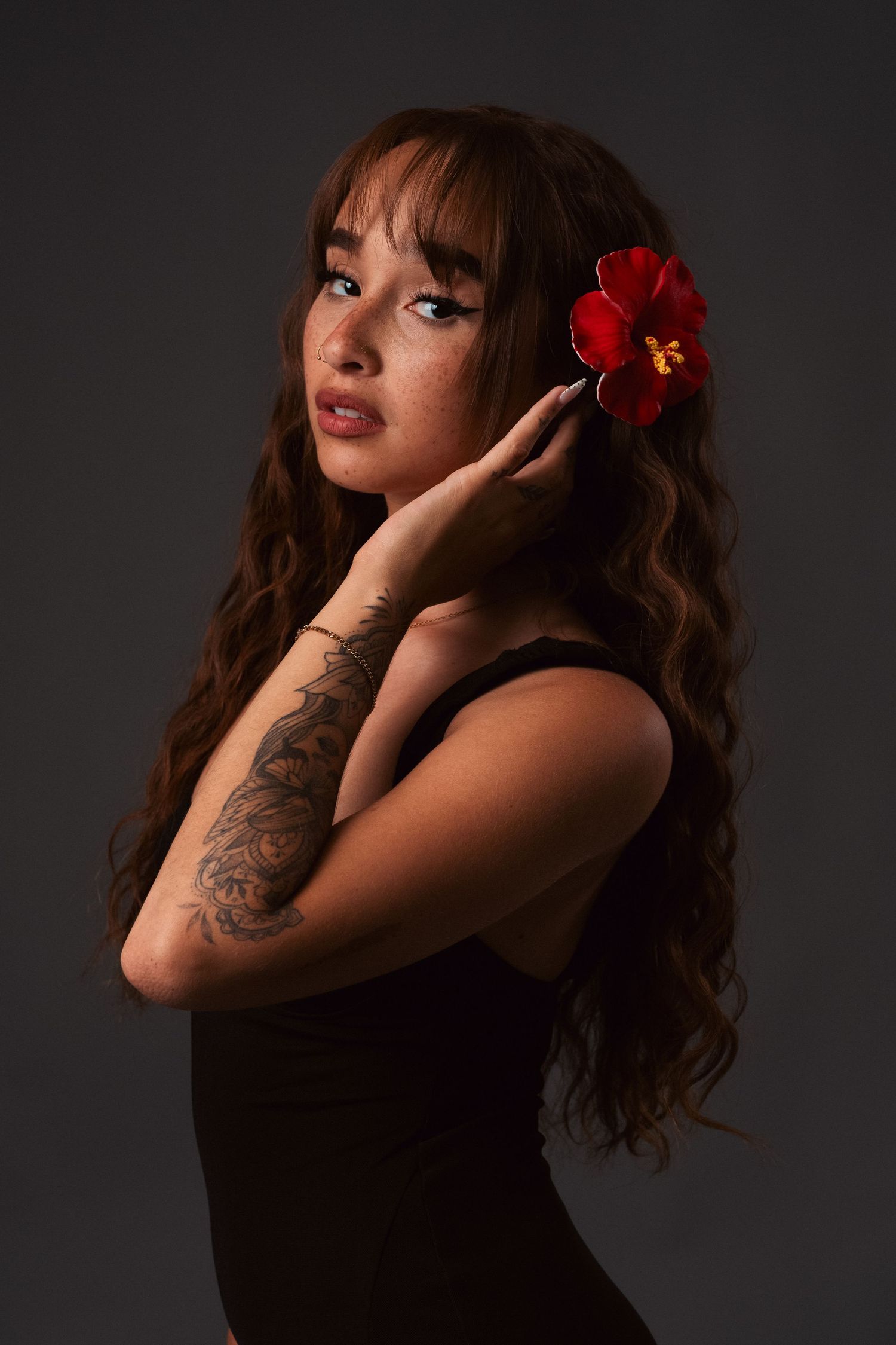 A moody studio portrait series showing a woman with dark hair and red flower accessories against a dark background.