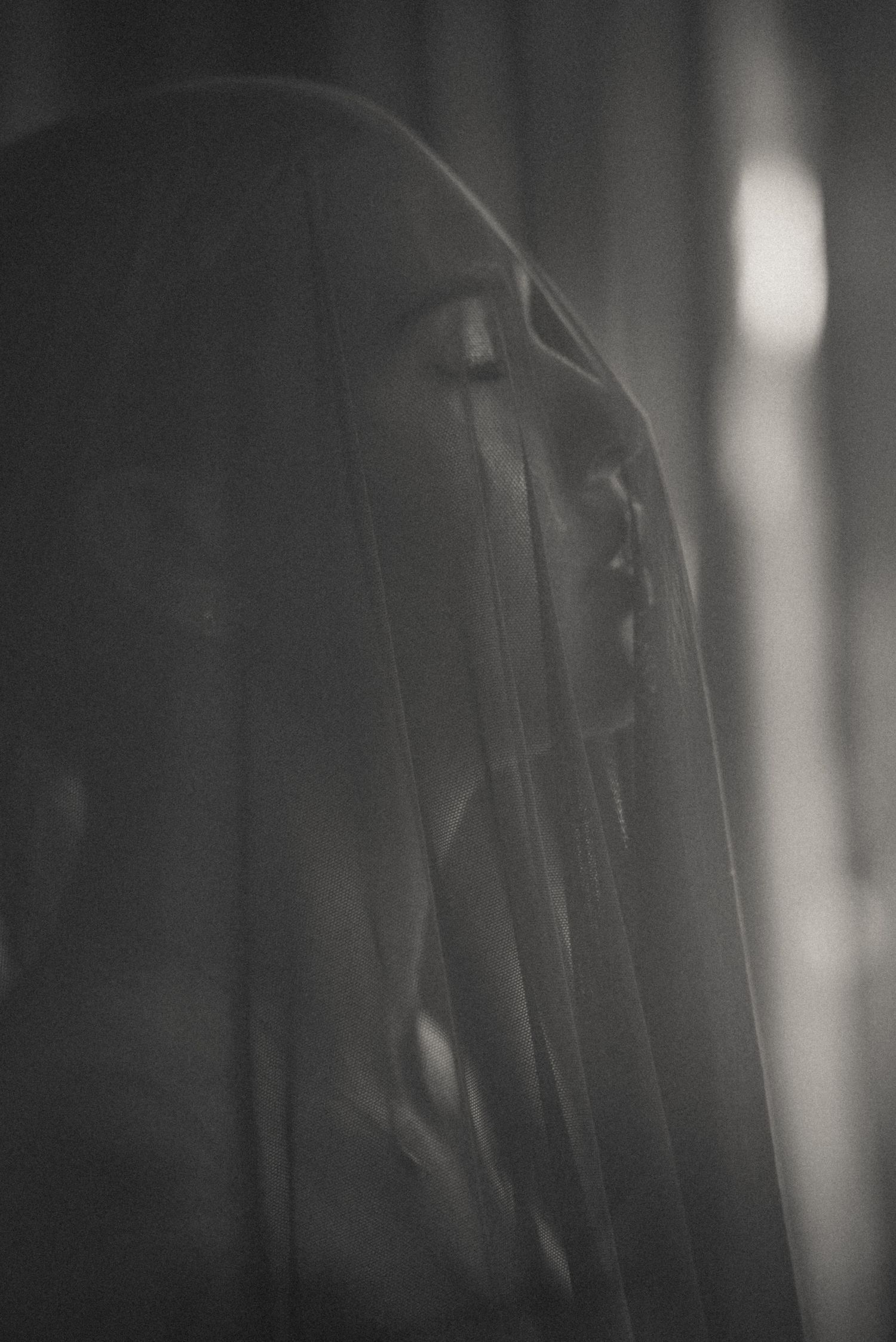 Abstract black and white photograph showing blurred vertical lines and shadows creating a moody atmospheric boudoir portrait.
