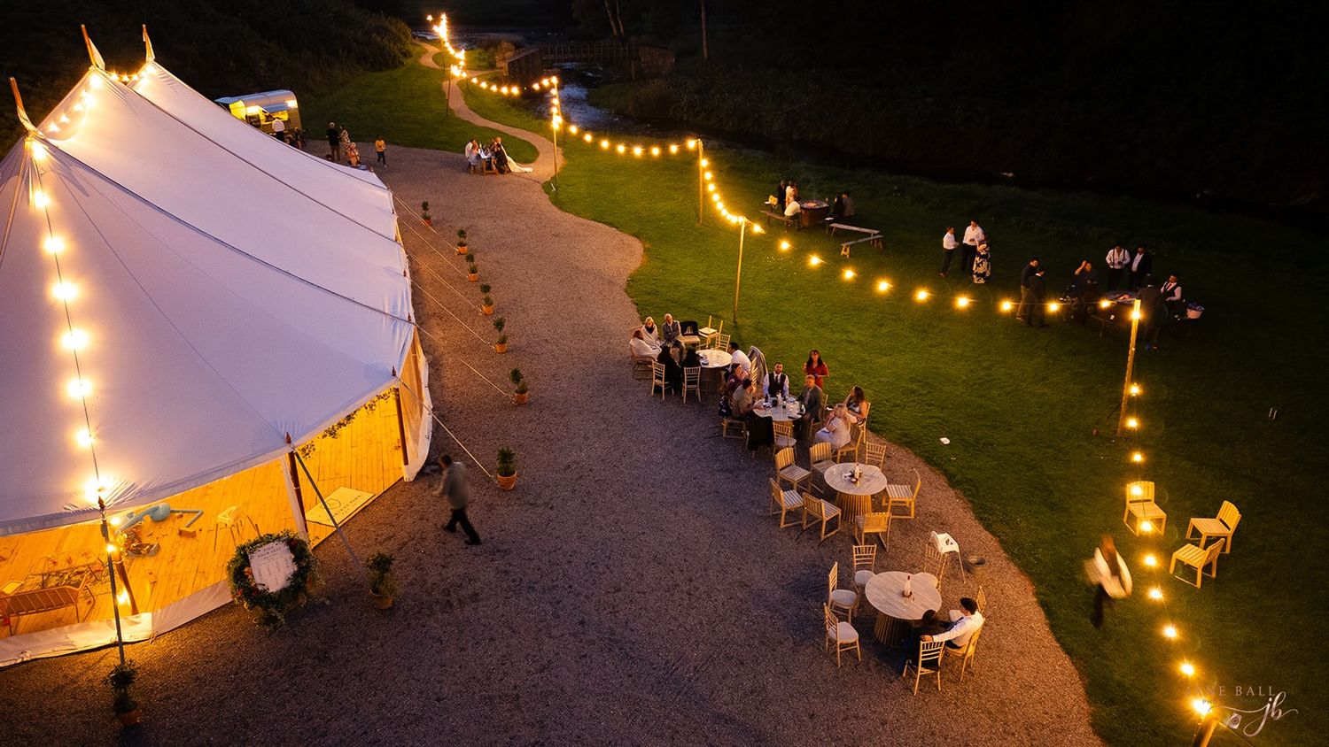 String lights illuminate an outdoor event space at night with white tents and tables set up for dining.