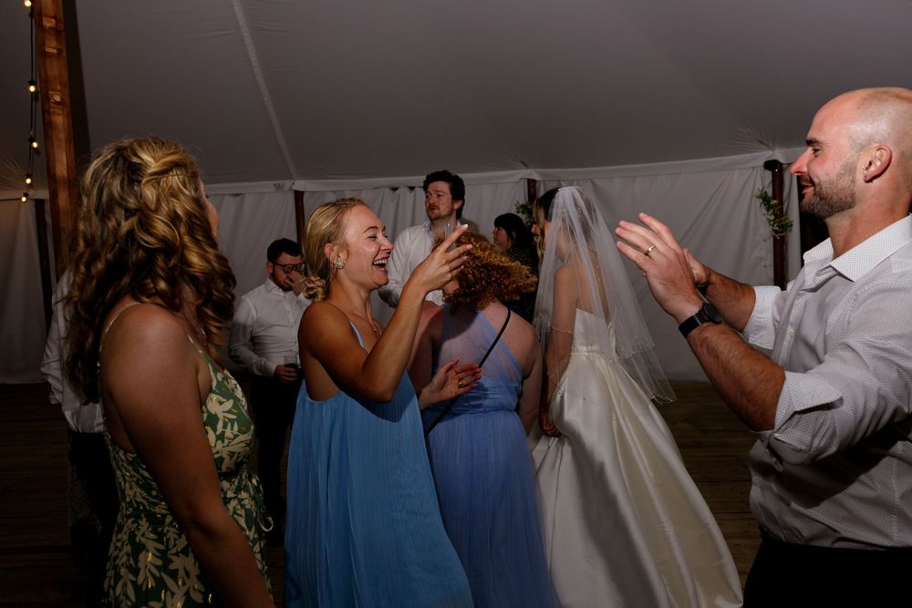 People dancing and celebrating at a wedding reception under a white tent with string lights.